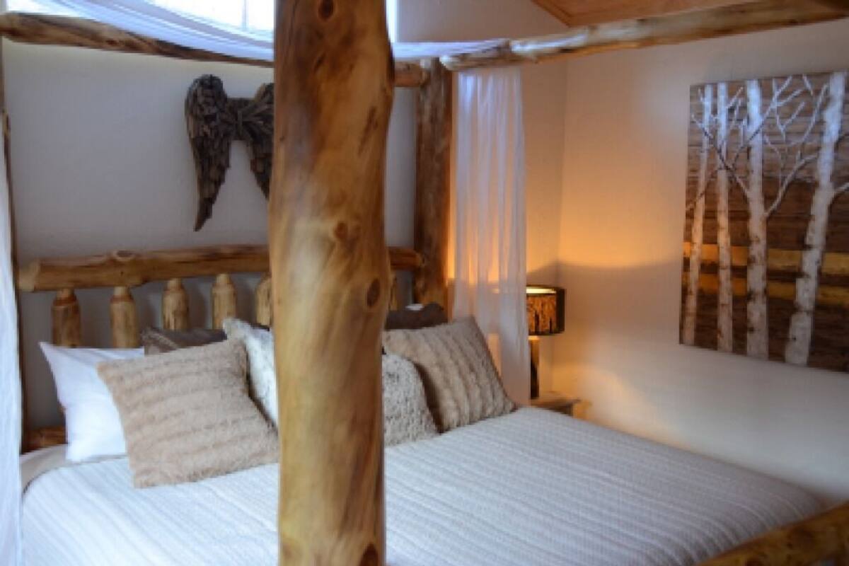 Un dormitorio con cabecera de madera, cama con ropa blanca y una lámpara fijada a la pared.