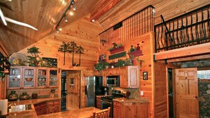 A wooden cabin interior with a kitchen, dining area, and a loft bedroom. - The Cabins at Country Road (Evergreen)