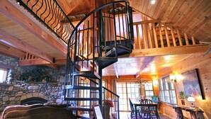 A wooden interior with a spiral staircase, stone fireplace, and a dining area with wooden furniture. - The Cabins at Country Road (Evergreen)