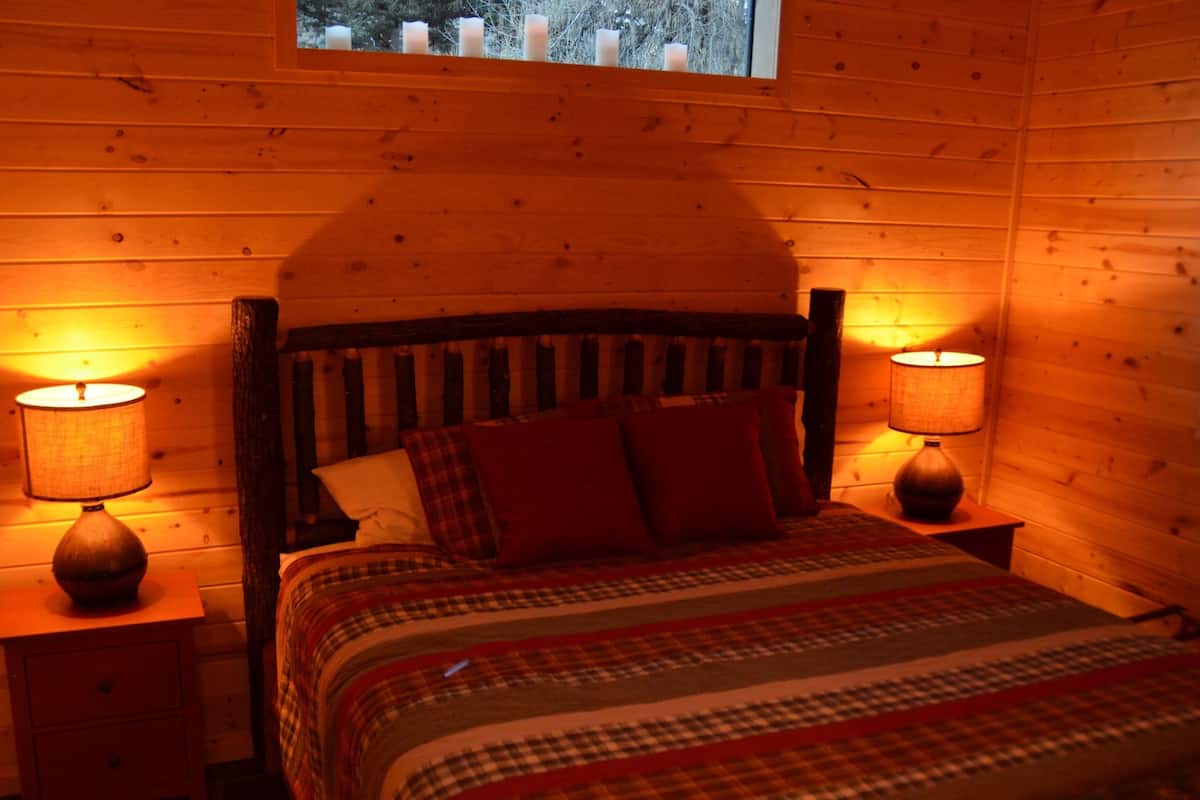Una habitación acogedora con una cama de madera, dos lámparas de noche y una ventana con velas.
