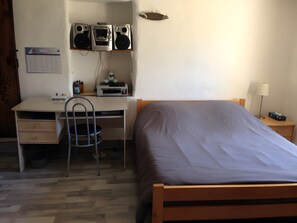 Ein Schlafzimmer mit einem Bett, einem Schreibtisch mit Stuhl, einem Drucker und einem Kalender an der Wand.