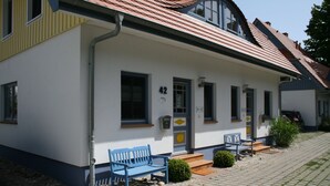 Un bâtiment blanc avec le numéro 42 sur la porte, un banc bleu et un petit espace aménagé en jardin.