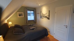 Une chambre à coucher avec un lit, des oreillers, une fenêtre avec des rideaux, une porte et des tableaux accrochés au mur.