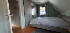 A bedroom with a bed, a wardrobe, a window with curtains, and a door.