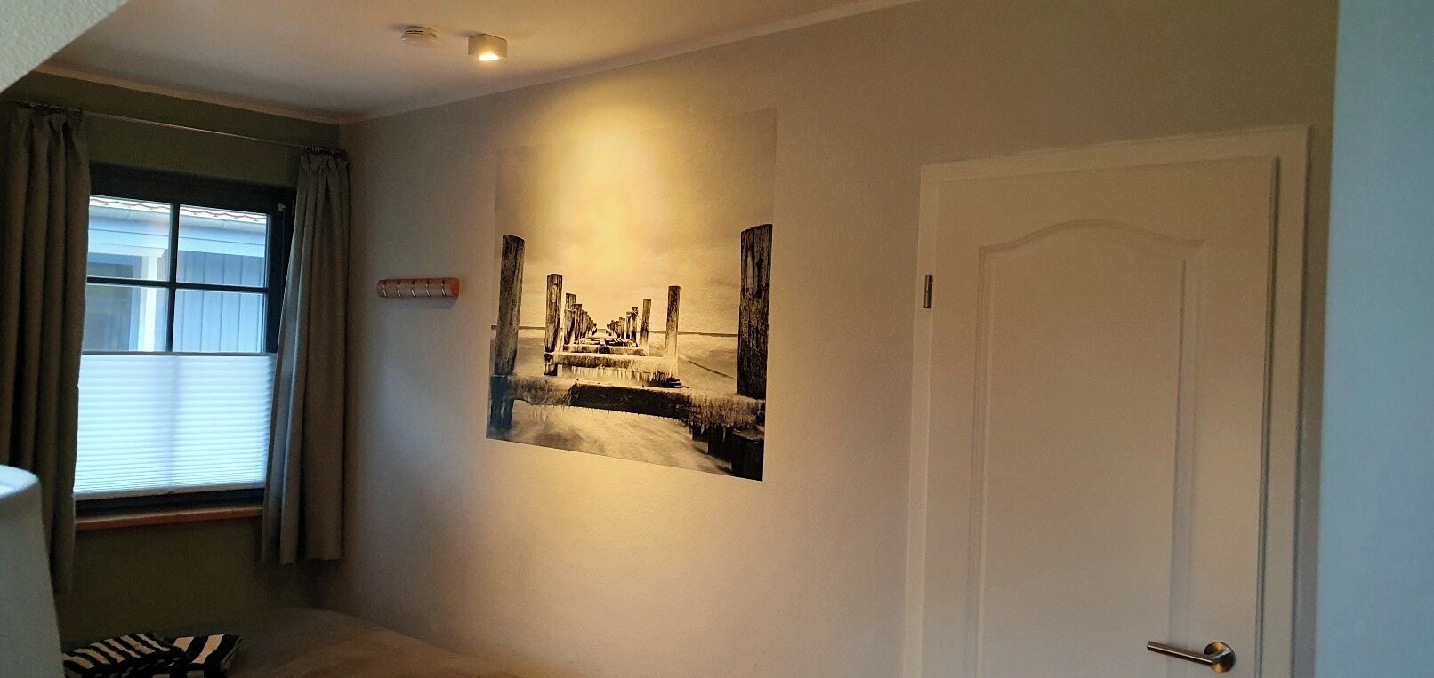 Un pasillo con una puerta, una ventana con cortinas y un cuadro colgado en la pared.