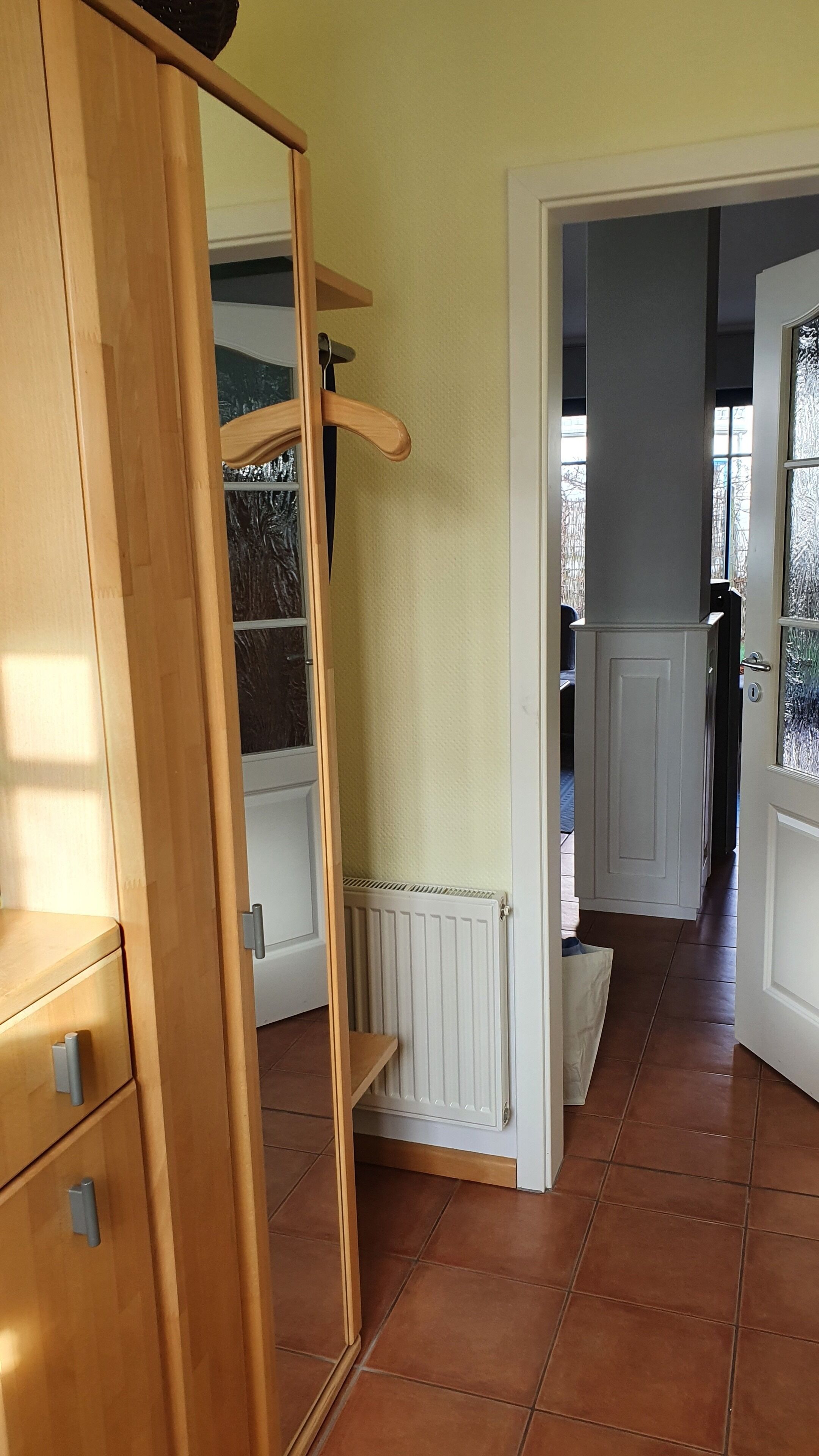 A hallway with a wooden wardrobe, a radiator, and a tiled floor.