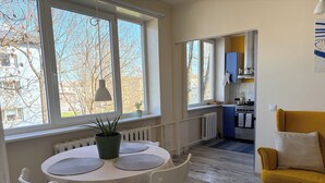 Un comedor con una mesa y sillas, una planta en maceta, y vistas a una cocina y al exterior.