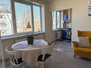 Un comedor con una mesa y sillas, una planta en maceta, y vistas a una cocina y al exterior.