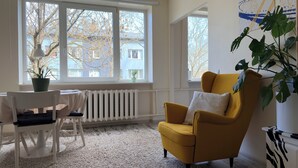 Una habitación con un ventanal grande, un sillón amarillo, un radiador blanco y una planta en maceta.