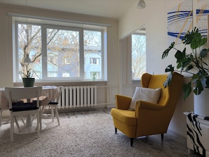 Una habitación con un ventanal grande, un sillón amarillo, un radiador blanco y una planta en maceta.