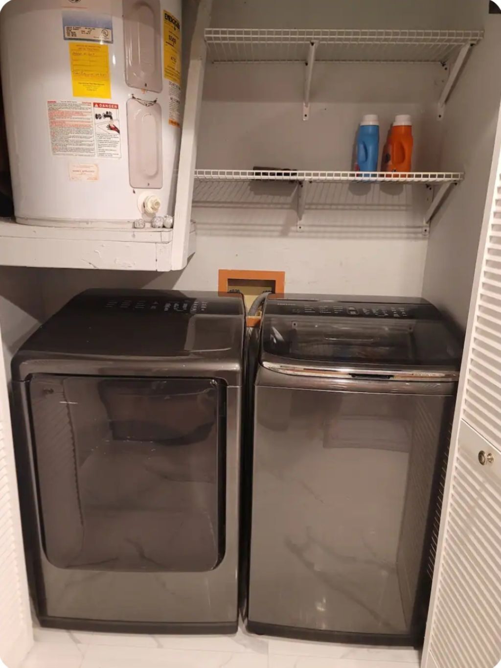 A laundry room with two stacked washers and dryers, a shelf with detergent bottles, and a water heater.