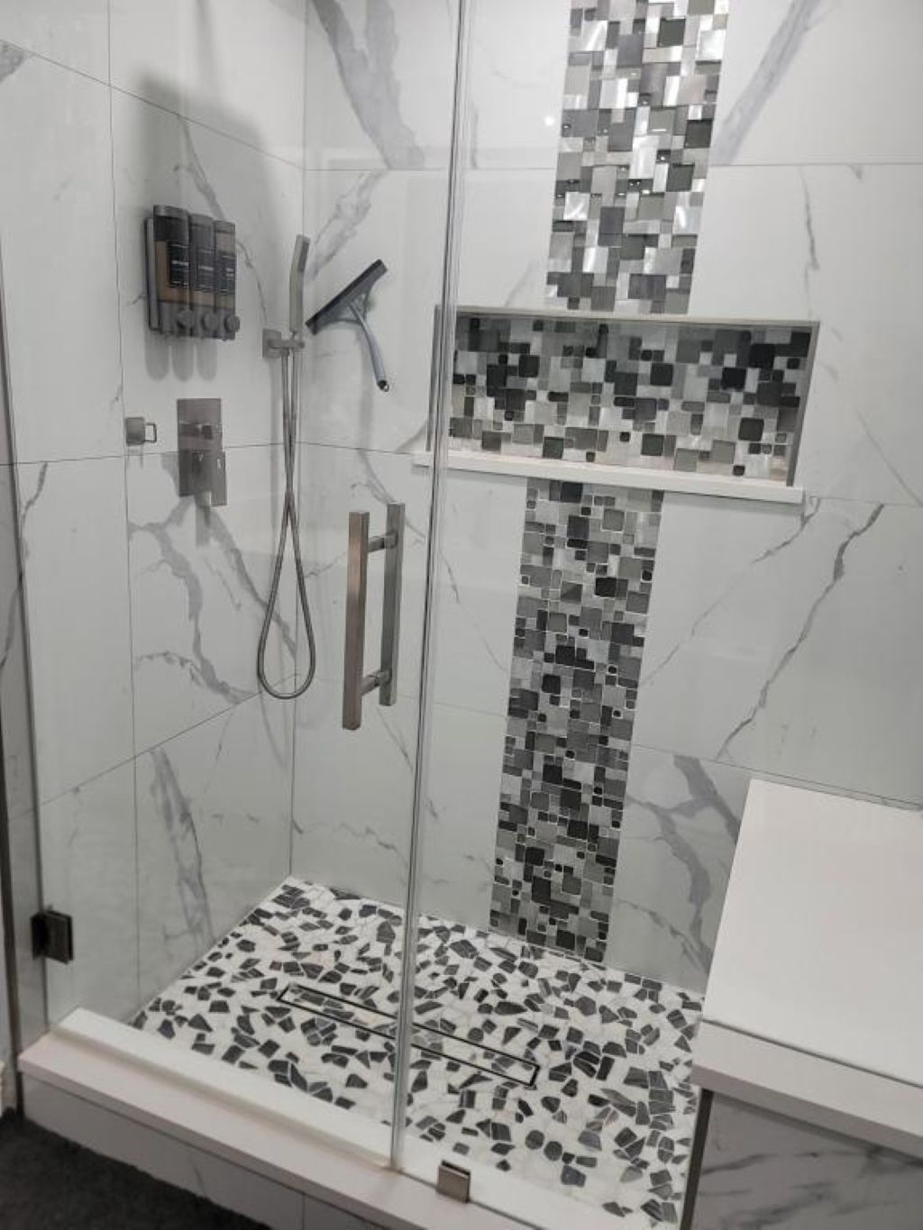 A shower with a glass door, a tiled wall, and a small shelf.