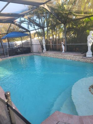 An outdoor swimming pool with a covered area, a statue, and a blue umbrella. - Stylish 3BR Pool Home Villa Frankely! (TAMPA)