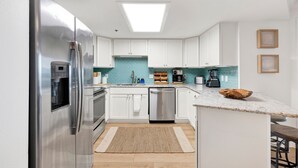 A modern kitchen with white cabinets, stainless steel appliances, a blue backsplash, and a skylight. - Island Pass OB • Steps to Beach • In the Heart of OB • Fully Loaded • Bunk Room (Orange Beach)