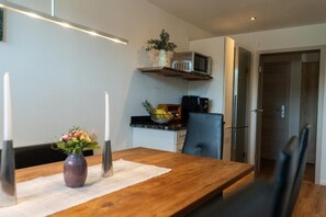 A modern dining area with a wooden table, two candles, and a vase of flowers.
