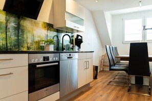 A modern kitchen with stainless steel appliances, a dining area with a black chair, and a window providing natural light.