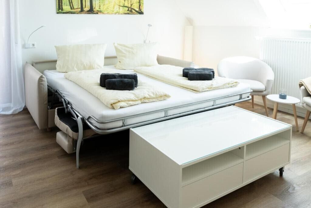 Une chambre moderne avec un lit convertible, une table de chevet blanche et une vue sur une forêt par la fenêtre.