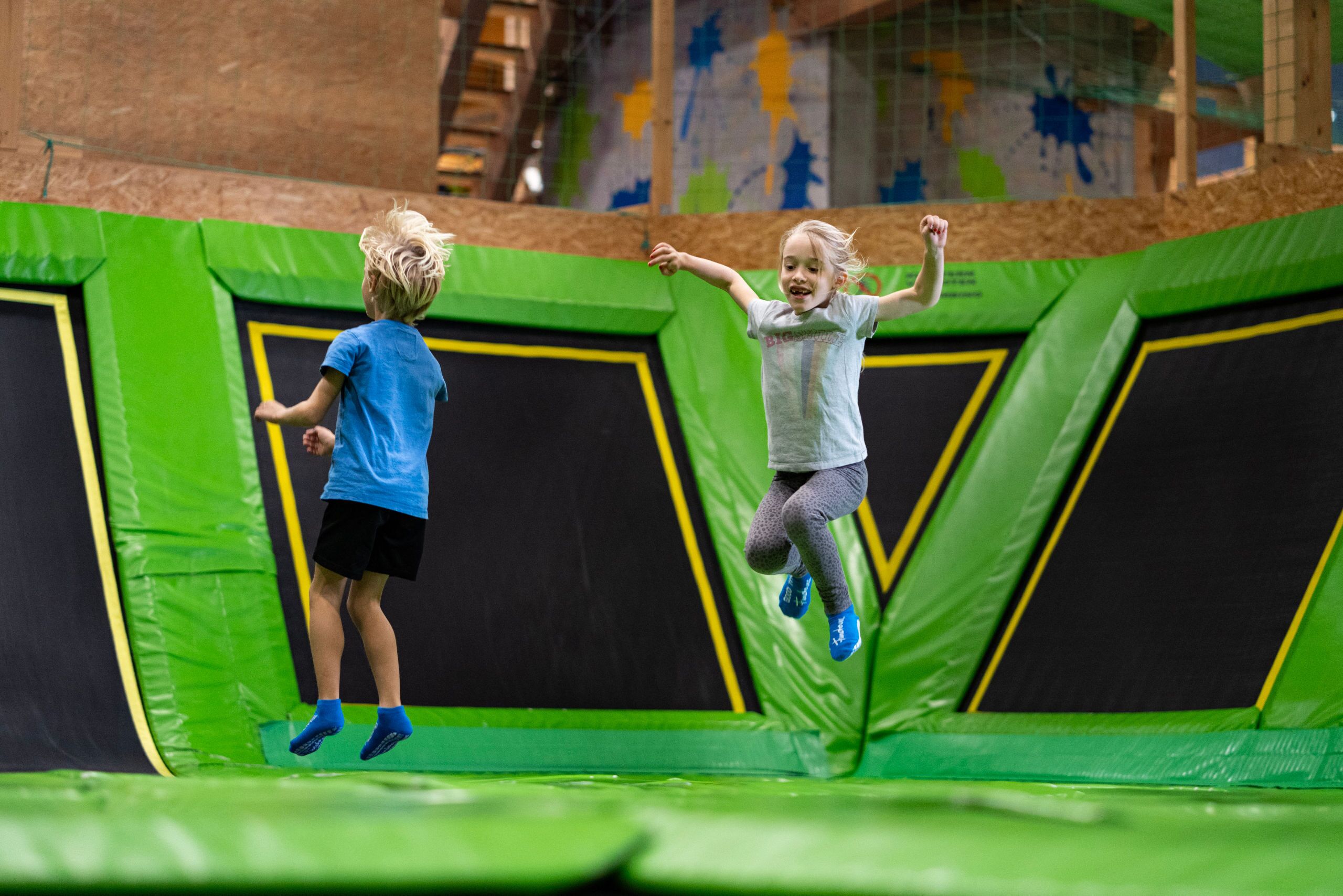 Zwei Kinder springen auf einem grünen Trampolin.
