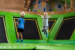 Two children jumping on a green trampoline.