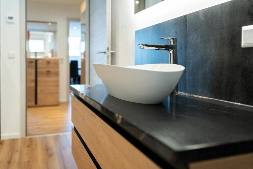 Une salle de bain moderne avec un lavabo sur colonne blanc, un plan de toilette foncé et un grand miroir.