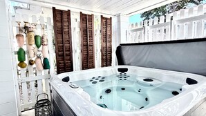 Ein Whirlpool mit weißer Außenverkleidung und Metallrahmen, umgeben von einem weißen Zaun mit braunen Fensterläden.