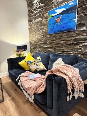 A dark blue sofa with a patterned throw blanket and a cushion with a floral design. A painting of a person in a blue swimsuit is on the wall. - Windermere Apartments - Long Term Rental Available (Windermere)
