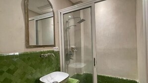 Un bany amb una paret de mosaic verd, un lavabo blanc, una cabina de dutxa de vidre i un sostre amb il·luminació empotrada.