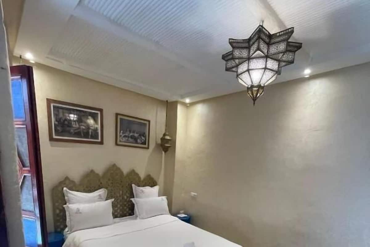A hotel room with a bed, a bench, a patterned rug, and two wall-mounted pictures.