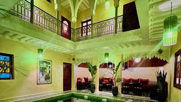 Zona d'una piscina interior de diversos nivells, amb sòl de rajola i una piscina central, envoltada de balcons i zones d'estar.