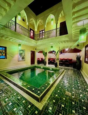 A multi-level indoor pool area with tiled flooring and a central pool, surrounded by balconies and seating areas. - RIAD NAFFAR (Marrakech)