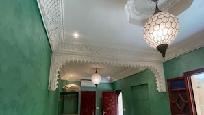 Una habitació amb parets verdes, un llit amb llençols blancs, una cadira groga i una catifes amb dibuixos.