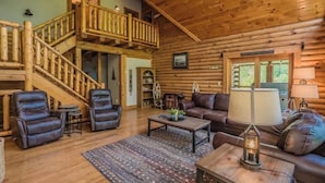 A log cabin interior with a staircase, leather sofas, a coffee table, and a lamp. - Luxury Cabin with Private Waterfall & Hot Tub (Sevierville)