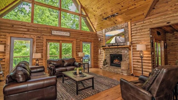 A log cabin interior with a fireplace, leather furniture, and large windows. - Luxury Cabin with Private Waterfall & Hot Tub (Sevierville)