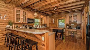 A log cabin interior with a kitchen, bar area, and wooden flooring. - Luxury Cabin with Private Waterfall & Hot Tub (Sevierville)