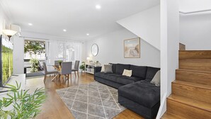Una sala de estar moderna con un sofá gris oscuro, una escalera de madera y un comedor con sillas y una mesa.