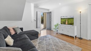 Una sala de estar moderna con un sofá modular gris oscuro, un tapete estampado, un televisor de pantalla plana sobre un mueble blanco y una lámpara de pie.