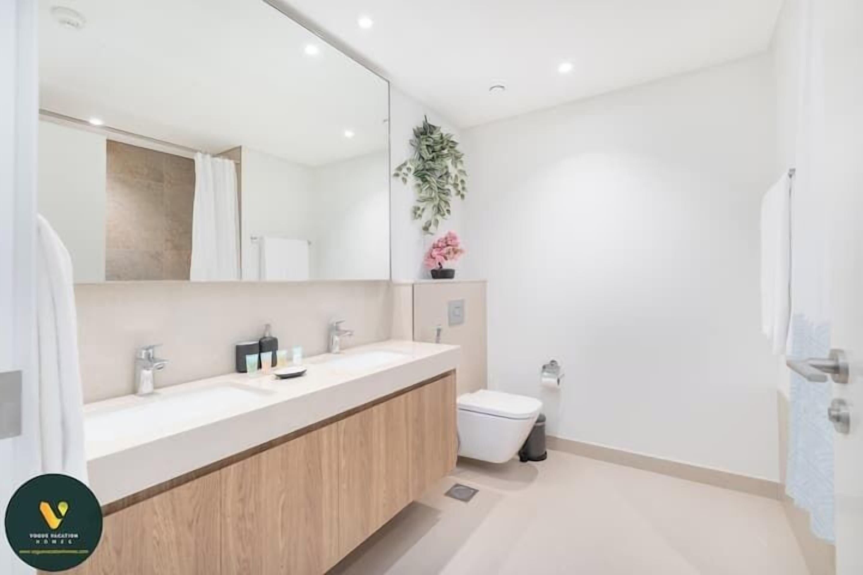 Un baño moderno con un espejo grande, dos lavamanos, un inodoro y un cubo de basura.