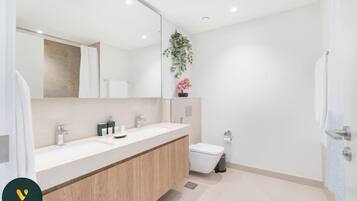 Un baño moderno con un espejo grande, dos lavamanos, un inodoro y un cubo de basura.