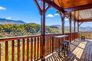 A wooden deck with tables and chairs overlooking a forested mountain range. - Sleeps 30: Amazing Views! Perfect for Groups! (Gatlinburg)