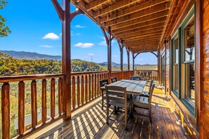 A wooden deck with a table and chairs, overlooking a mountainous landscape. - Sleeps 30: Amazing Views! Perfect for Groups! (Gatlinburg)