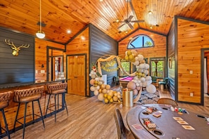 A spacious room with wooden walls and ceiling, a bar area with stools, and a dining table set for a game. - Sleeps 30: Amazing Views! Perfect for Groups! (Gatlinburg)