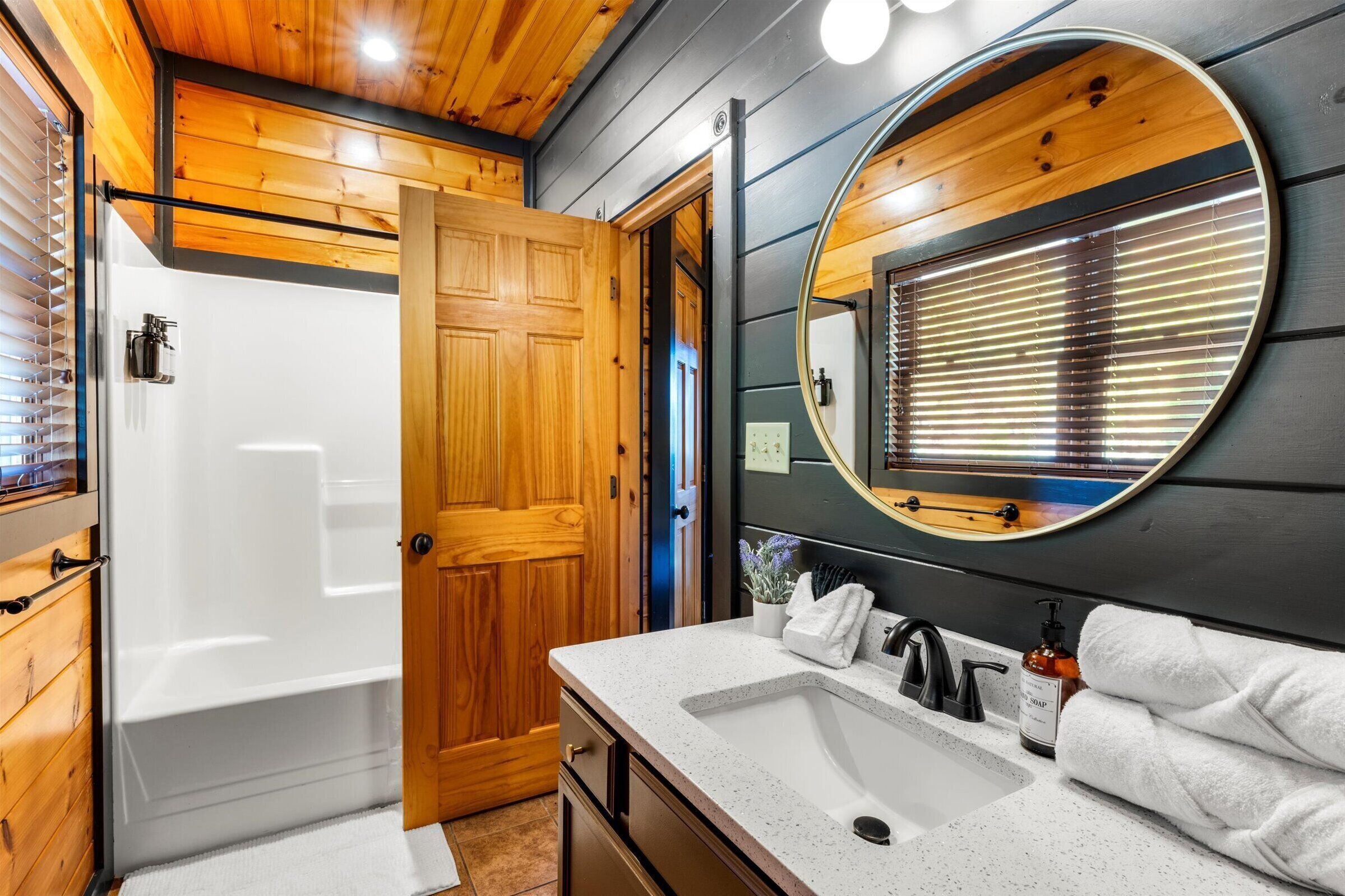 A bathroom with a wooden door, a bathtub, a sink with a mirror, and a towel rack.