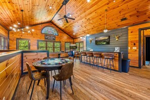 A wooden interior with a bar area, a dining table with chairs, and a ceiling fan. - Sleeps 30: Amazing Views! Perfect for Groups! (Gatlinburg)