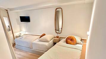 Een slaapkamer met twee bedden, een aan de muur bevestigde televisie, een plafondlamp en een spiegel.