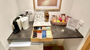 Une petite cuisine équipée d’une machine à café, de verres à vin, d’un panier de fruits et d’un tableau encadré au-dessus du comptoir.