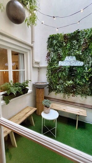 Une petite cour avec une pelouse artificielle verte, un banc en bois, une petite table et un jardin vertical portant l’inscription « Suite Patio A&A ».