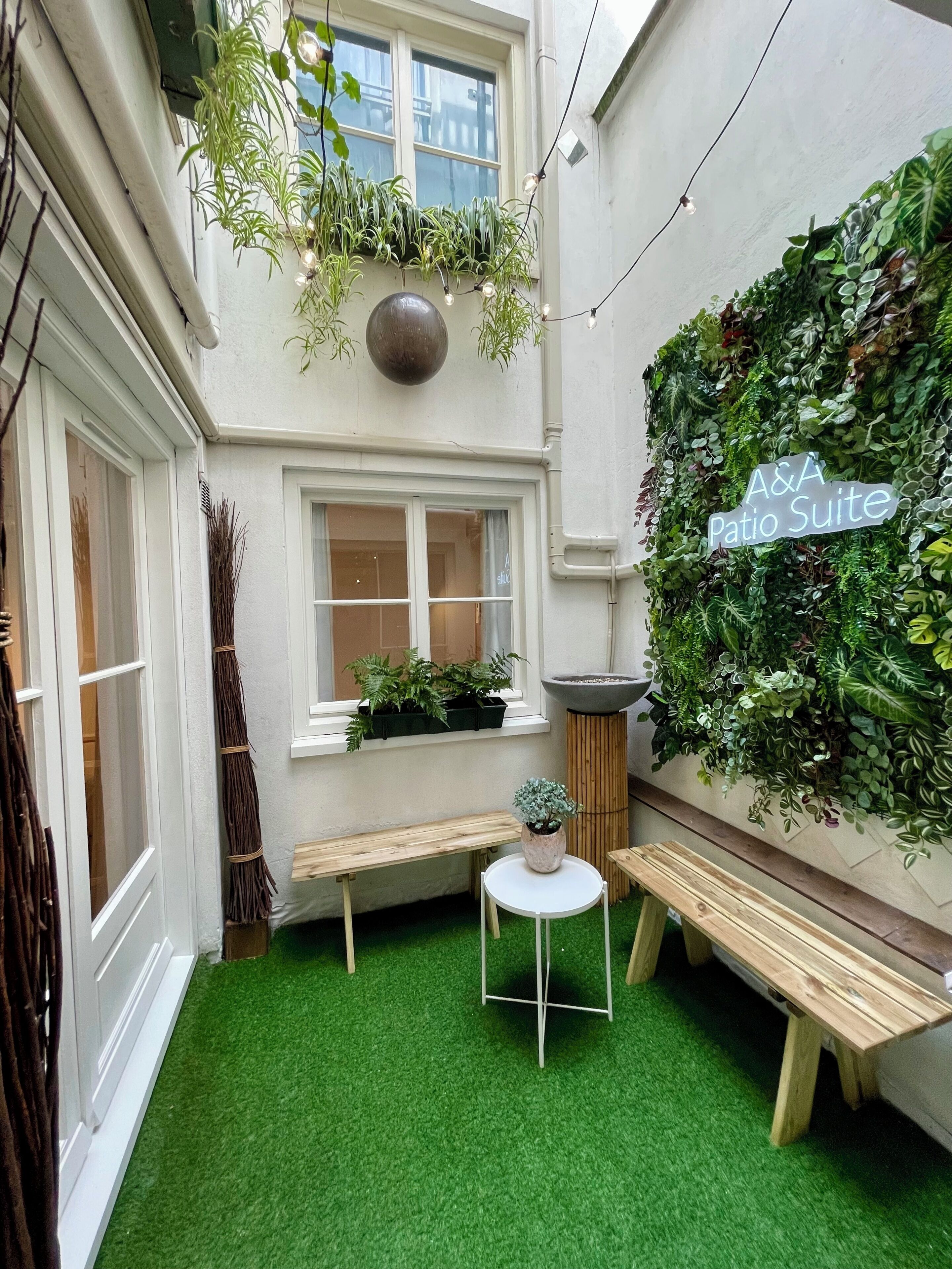 A courtyard with artificial grass, a wooden bench, a small table, and a wall covered in plants.