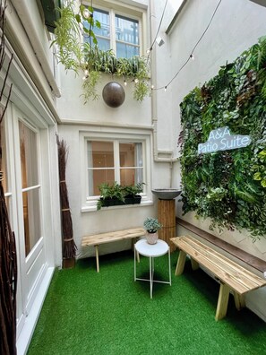 A courtyard with artificial grass, a wooden bench, a small table, and a wall covered in plants. - A&A Patio Suite (Amsterdam)