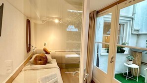 Une chambre d’hôtel comprenant un lit, une table de chevet, un miroir et donnant sur l’espace extérieur grâce à une porte vitrée.