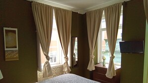 Une chambre d’hôtel avec un lit, des rideaux, un miroir, une commode et un téléviseur.